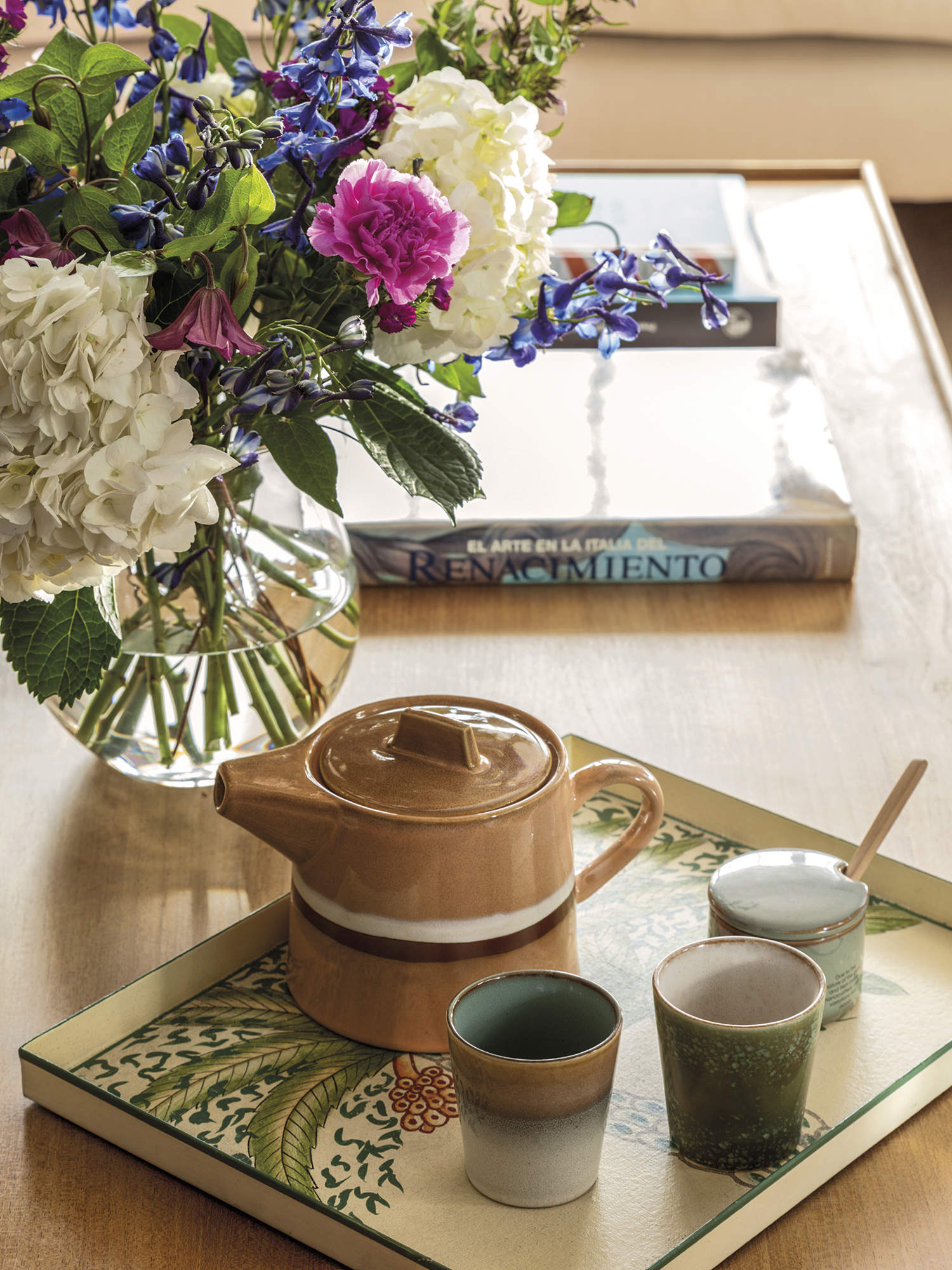 mesa de centro con bandeja con juego de té de cerámica, florero de cristal con flores